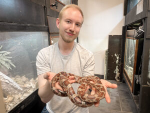 Jonathan som är engagerad i föreningen Alba håller upp en orm som ligger slingrad runt hans händer. 