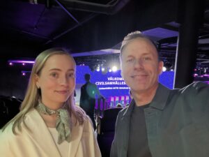 Två personer tar en selfie och ler in i kameran framför scenen.