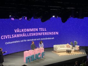 Bild på scenen där två personer står vid varsitt talarbord.