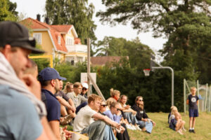 På bilden syns många deltagare sittandes i gräset under välkomnandet. 