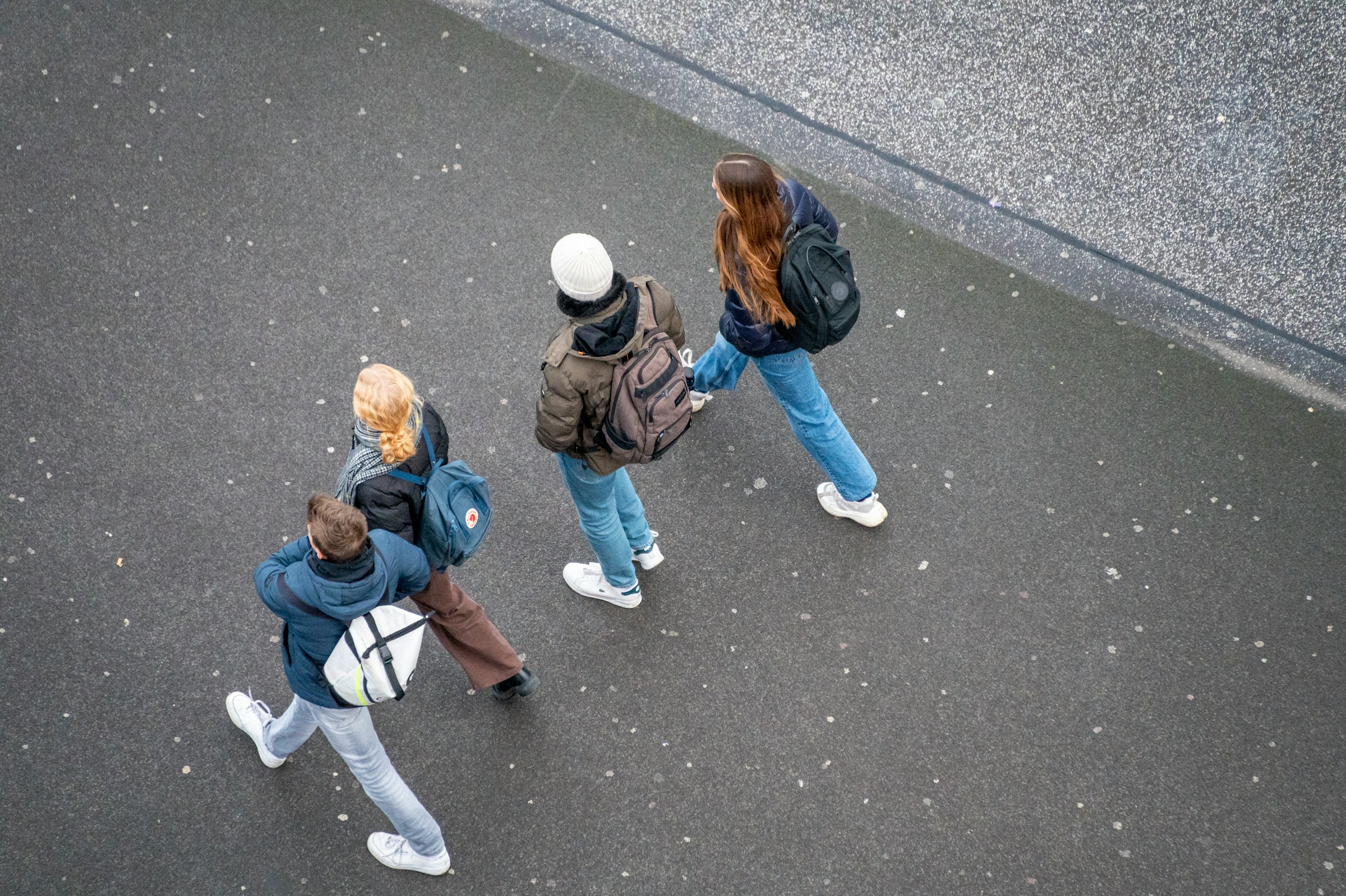 Fyra unga personer går tillsammans på en asfalterad väg, fotograferade ovanifrån.