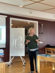 En kvinna står framför en grupp och presenterar. 